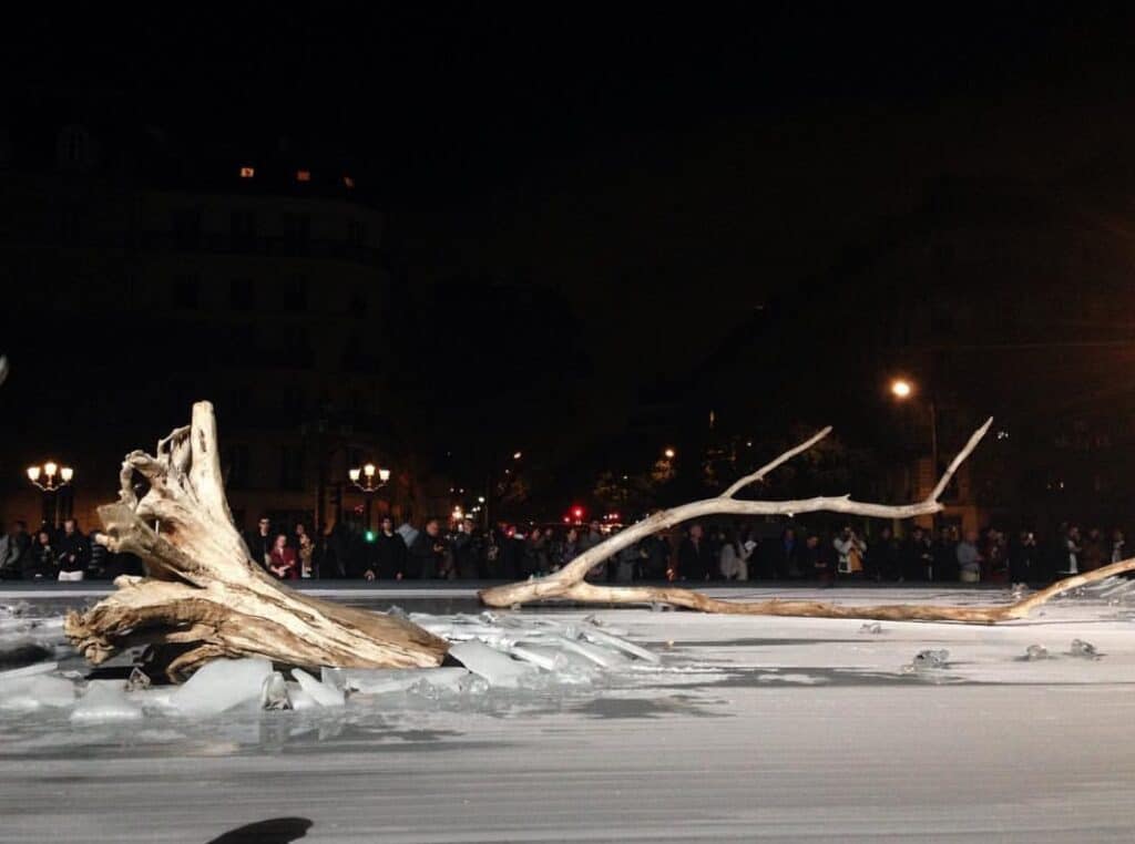 Installation Artistique de Troncs et Glace de Nuit Souche de bois flotté et blocs de glace lors d'une installation artistique nocturne devant une foule en ville.