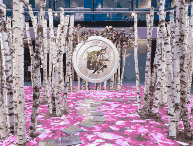 Installation Swatch Galeries Lafayette : Forêt de Bouleaux Journée Presse Swatch aux Galeries Lafayette : forêt de bouleaux et pétales roses autour d'une horloge géante centrale.
