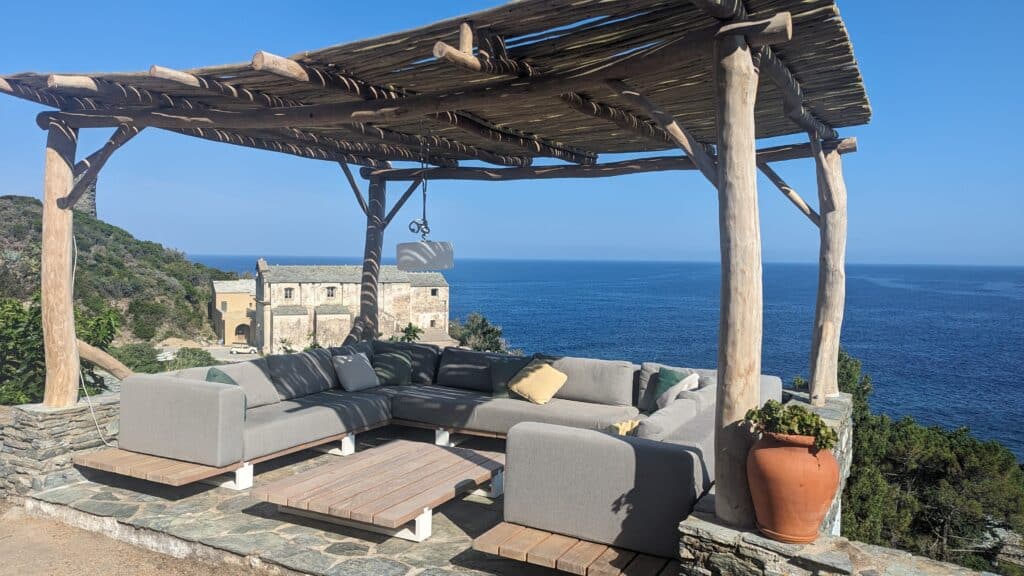Terrasse de Luxe avec Vue Panoramique sur la Méditerranée Terrasse avec canapés gris sous pergola en bois, vue imprenable sur la mer Méditerranée et un ancien bâtiment en pierre.