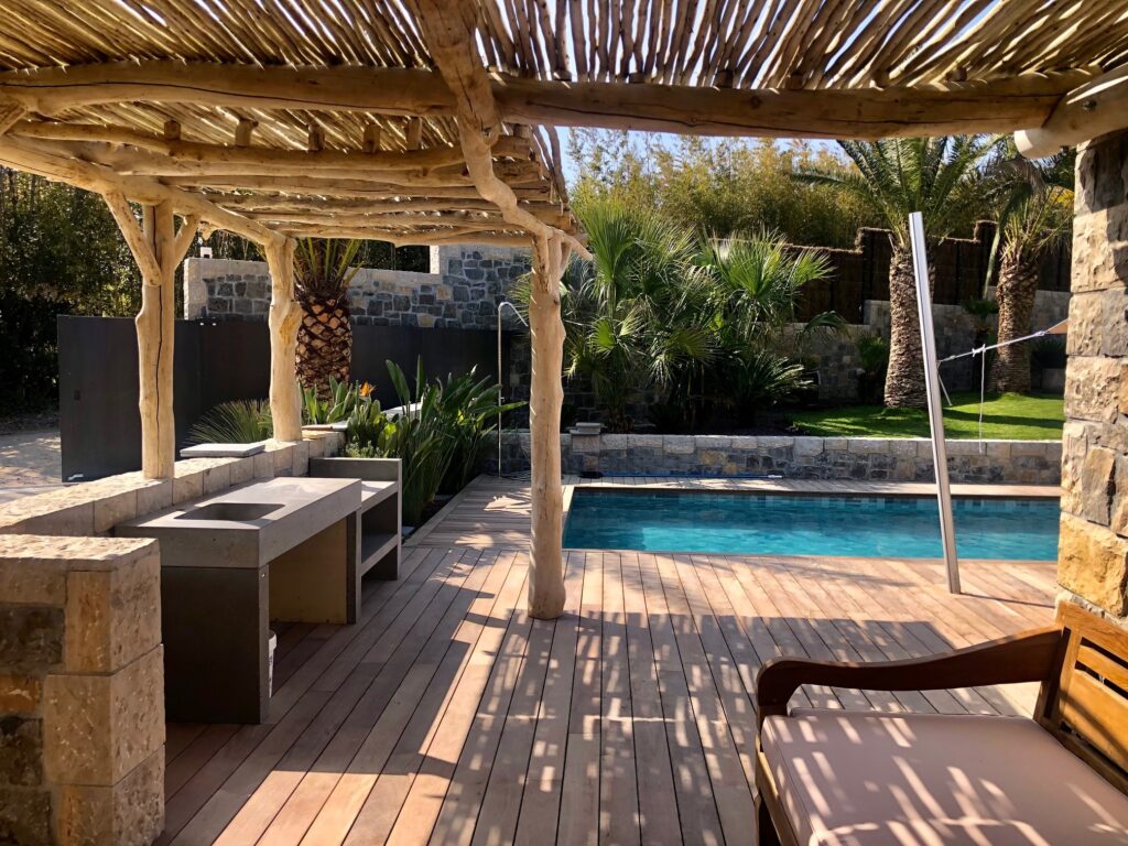 Aménagement terrasse avec pergola rustique et piscine Terrasse avec pergola rustique, piscine et cuisine d'été entourées de palmiers tropicaux.