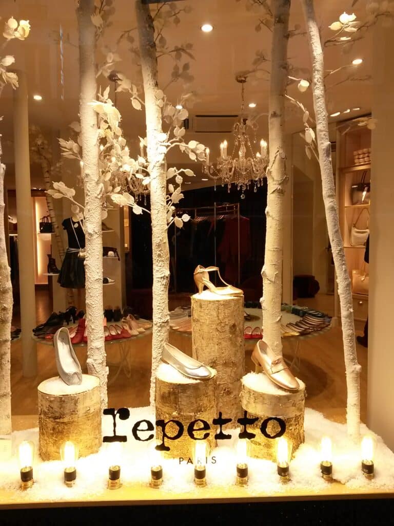 Vitrine Repetto Paris : Chaussures de Luxe et Décor Hivernal Vitrine hivernale Repetto Paris avec chaussures de luxe sur troncs de bois et décor de bouleaux enneigés.